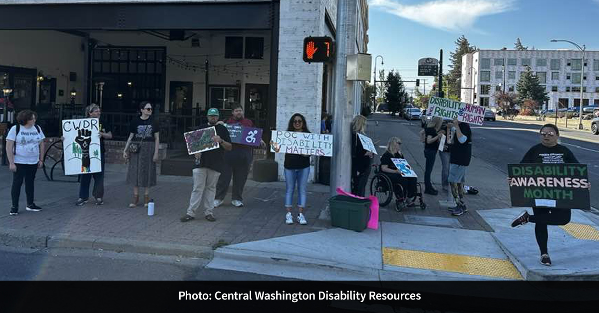 About 10 people holding disability rights signs standing along a sidewalk.