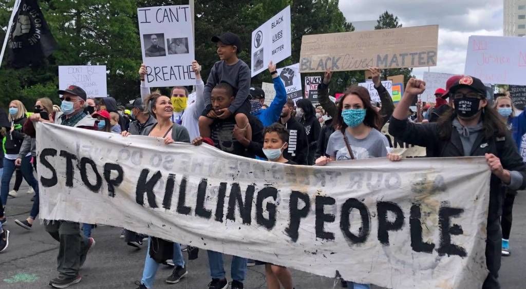 A group of people marching in the streets holding a banner that reads, “Stop Killing People.”