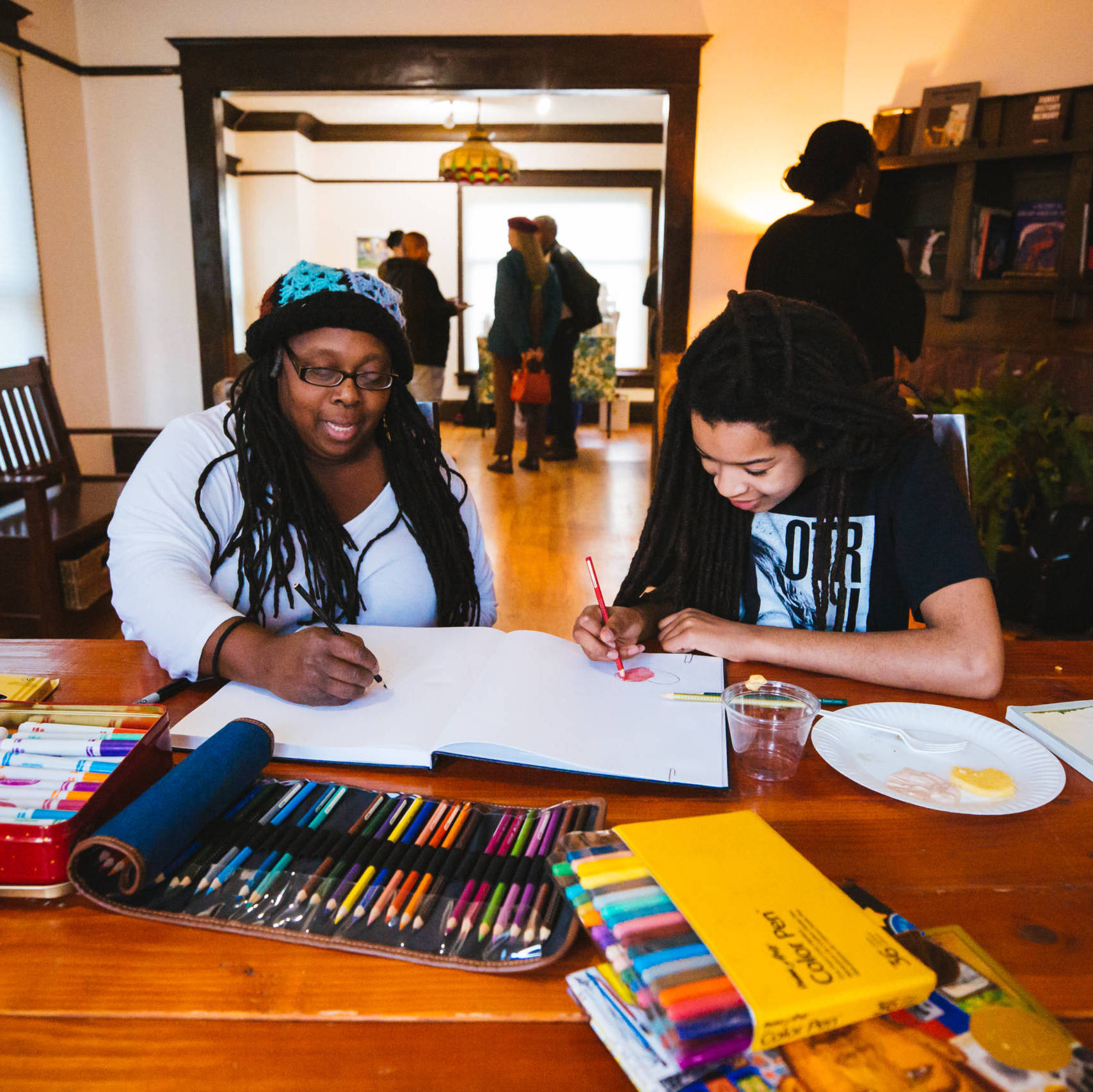 Two Black people inside a Central District home coloring with pencils into a book.