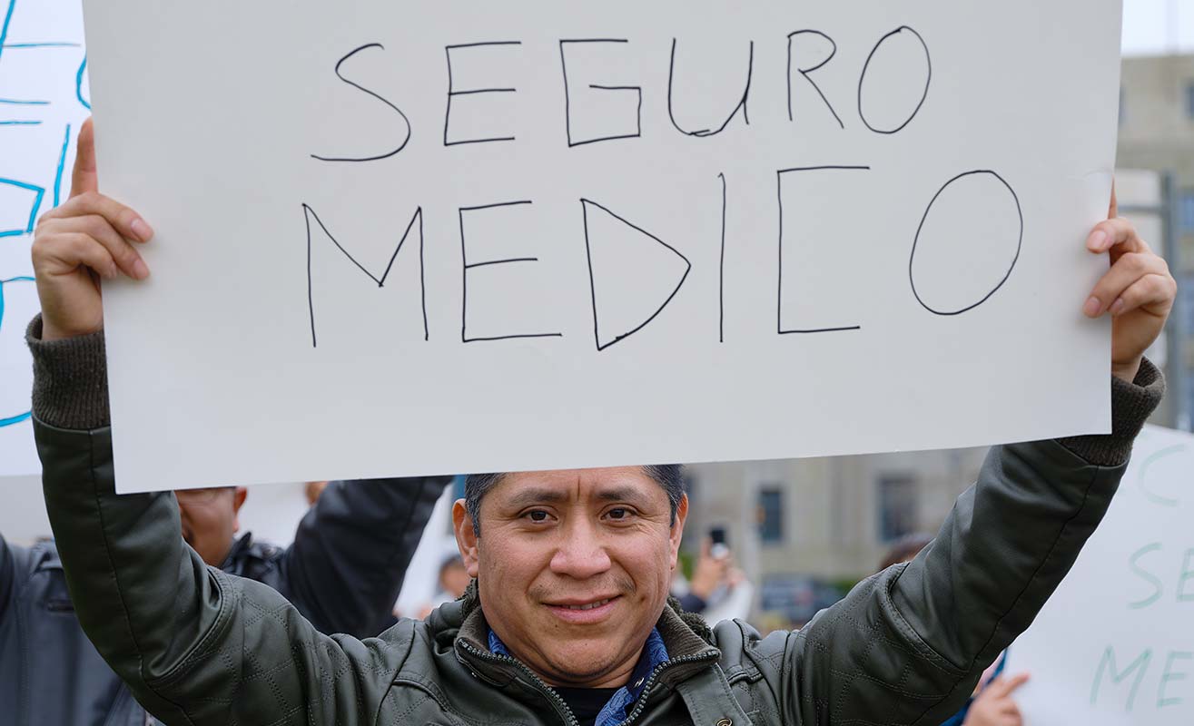 A person holding up a sign in partial view that reads, seguro medico.