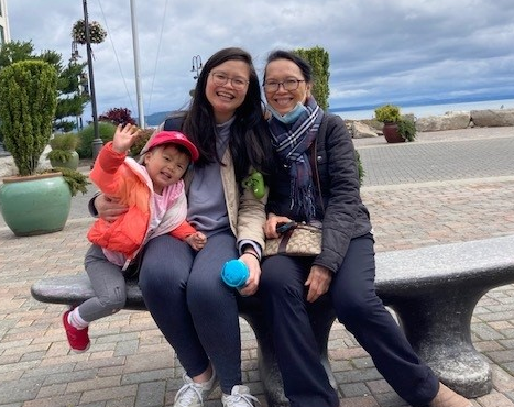A baby, her mom, and her mom’s mom sit on a bench at a waterfront.