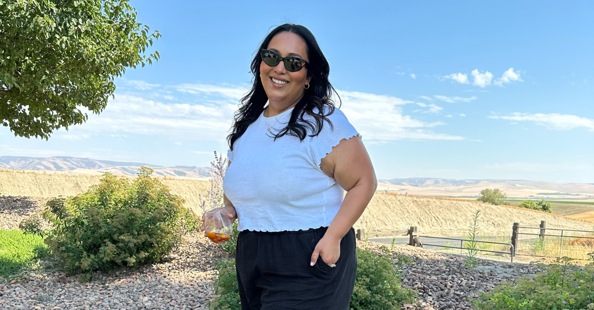 Adanna stands in front of a blue sky and scenic landscape.